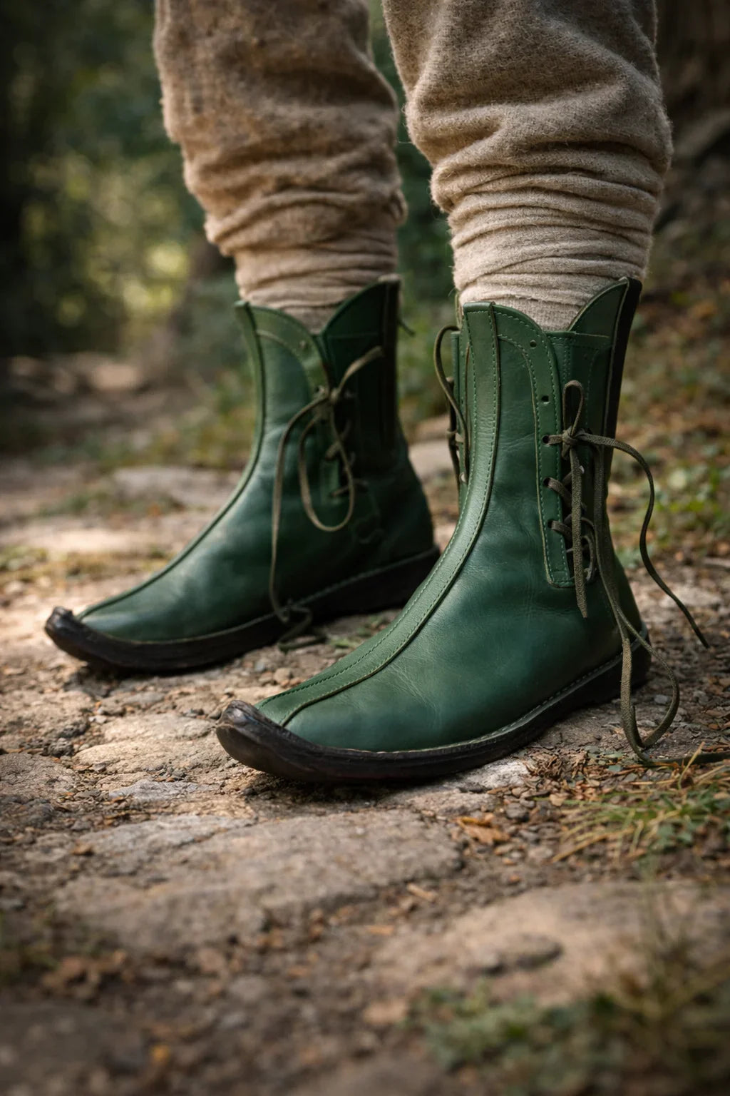 Green medieval leather boots with wrap laces, worn on a forest path for LARP or SCA reenactment.
