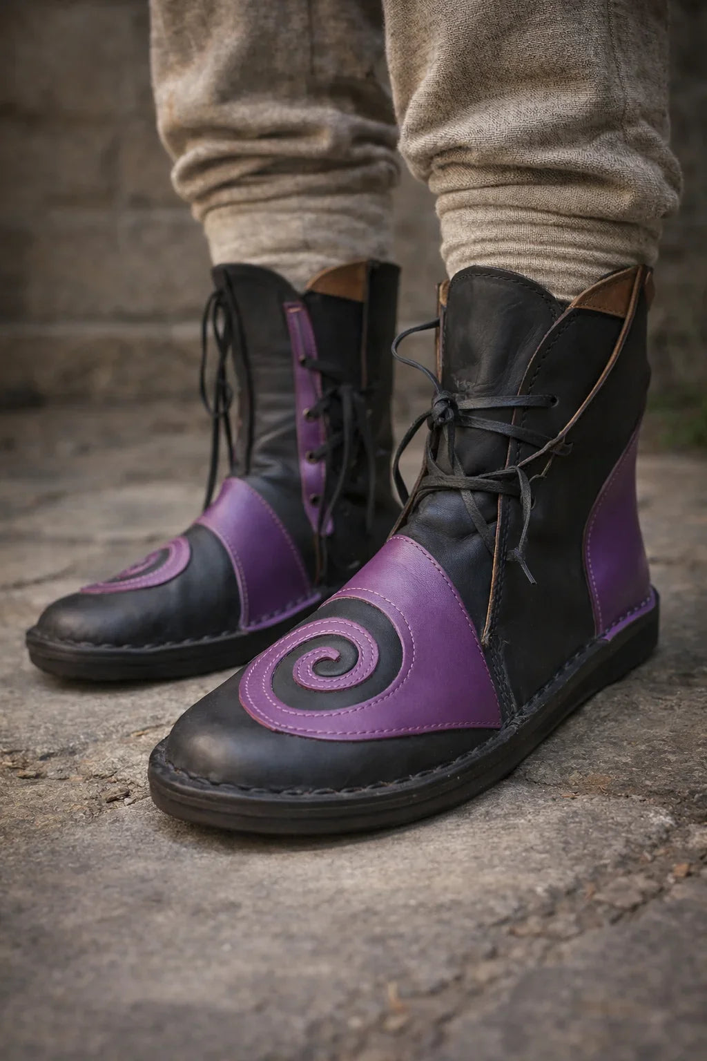 Black and purple medieval leather boots with spiral design, wrap laces, and full-grain texture, worn for LARP or Renaissance faire.